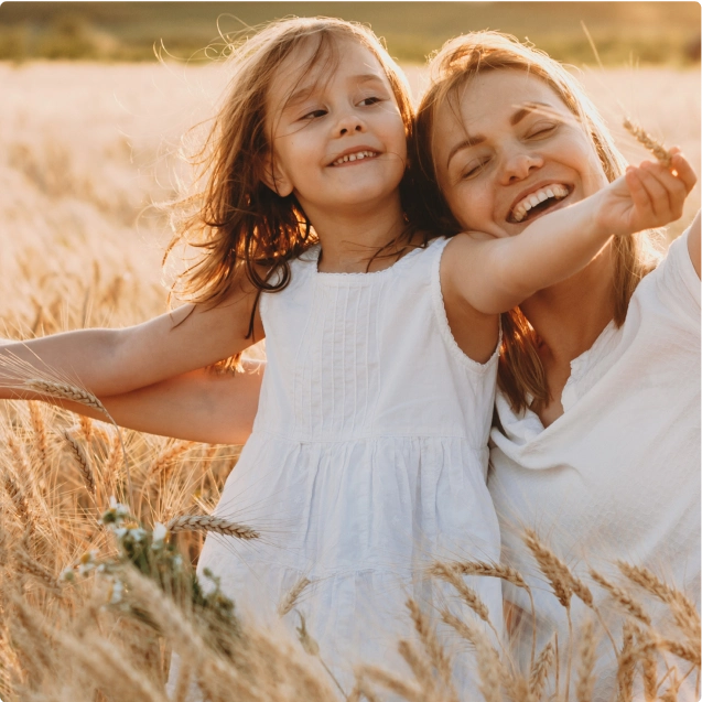 A mother and daughter smiling in a field of tall grass.